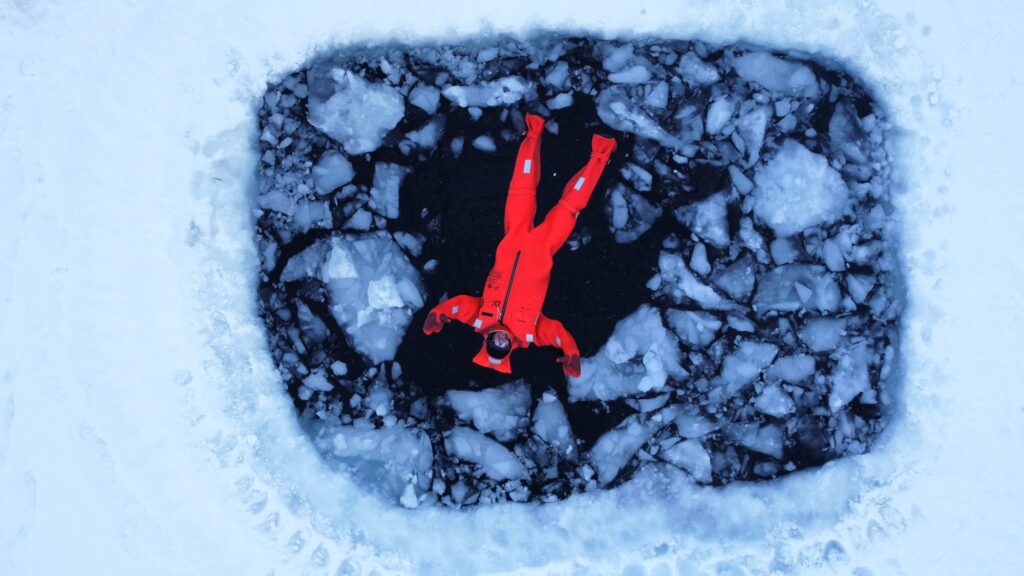Aerial view of a person in an aquata immersion suit floating in an ice hole